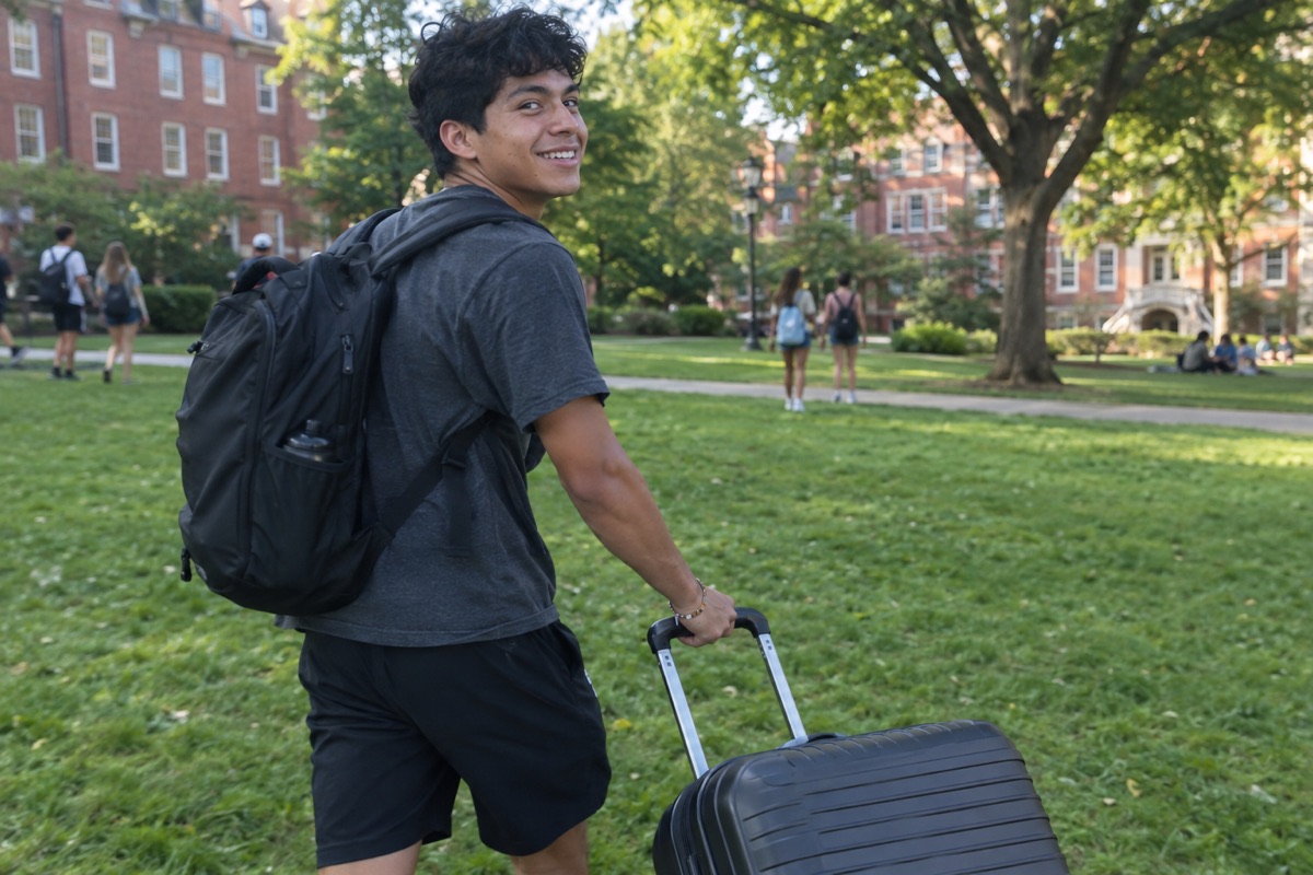 A student pulling a suitcase across a college lawn